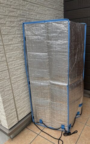 玄関前に置き配されたコープデリの荷物と銀色の保冷カバー